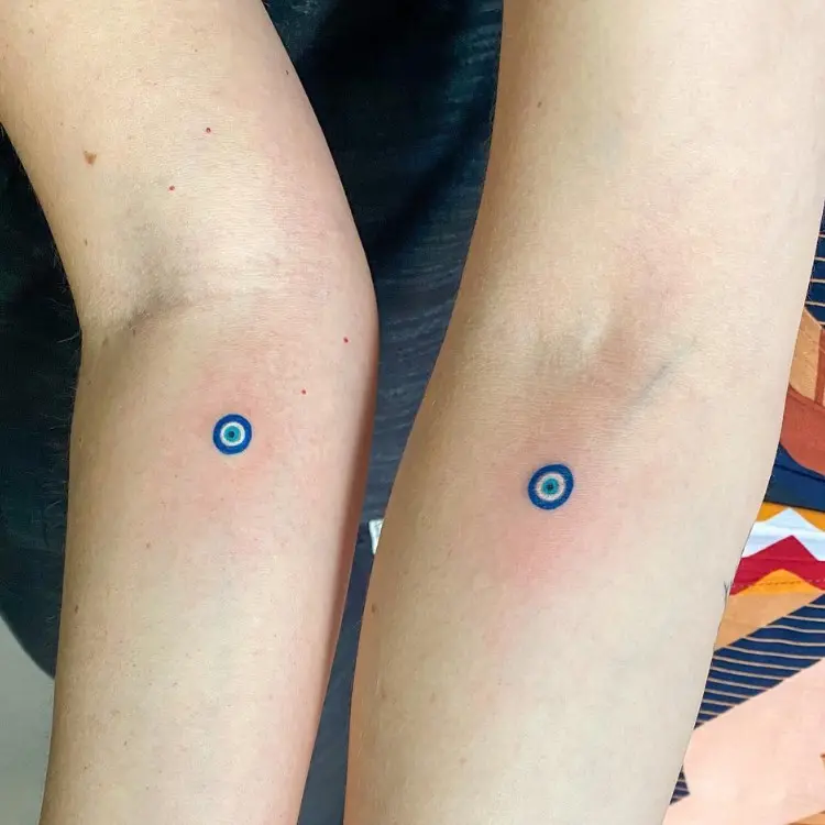 Braços com tatuagem de pequeno olho grego em azul e branco
