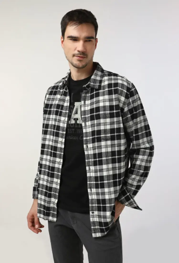 Homem usando camiseta preta estampada + camisa xadrez preta e branca + calça cinza escuro