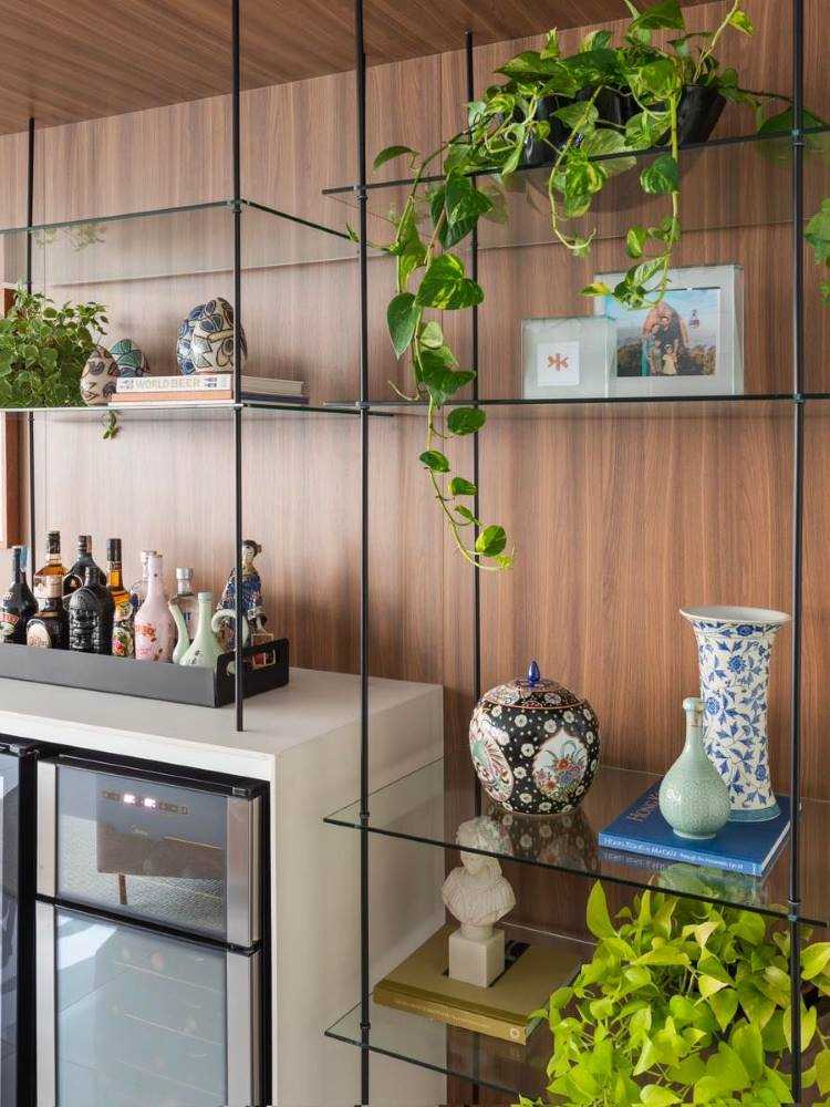 Estante de metal vazada com porta-retratos, vasos de porcelana, plantas e bandeja com bebidas. 