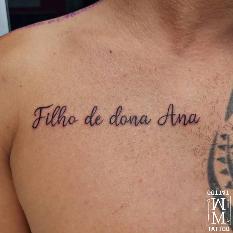 A imagem mostra o torso de um homem com uma tatuagem preta no peito que diz "Filho de dona Ana" em caligrafia cursiva. Parte de outra tatuagem preta pode ser vista no ombro direito do homem. No canto inferior direito, há um logotipo em branco com a palavra "TATTOO" invertida.








