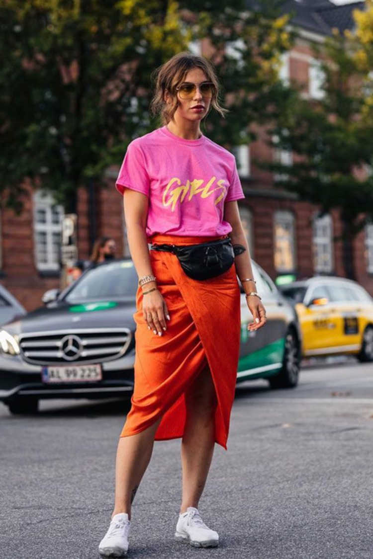 Mulher de pele clara com blusa rosa, saia midi laranja e tênis