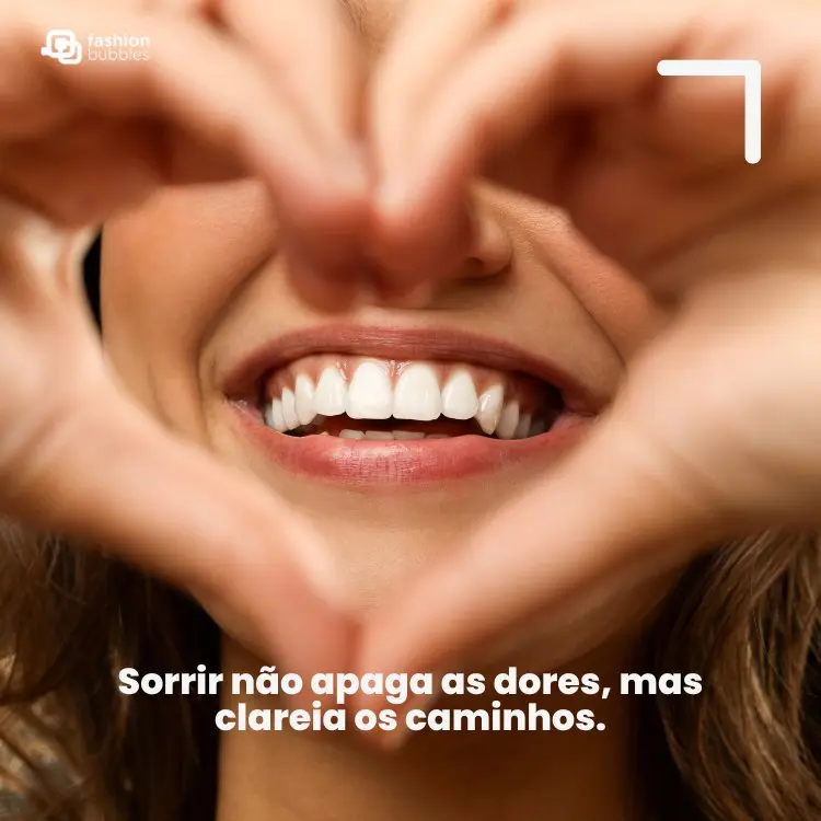 Mulher de pele clara sorrindo e fazendo coração com as mãos, além de frase: Sorrir não apaga as dores, mas clareia os caminhos.