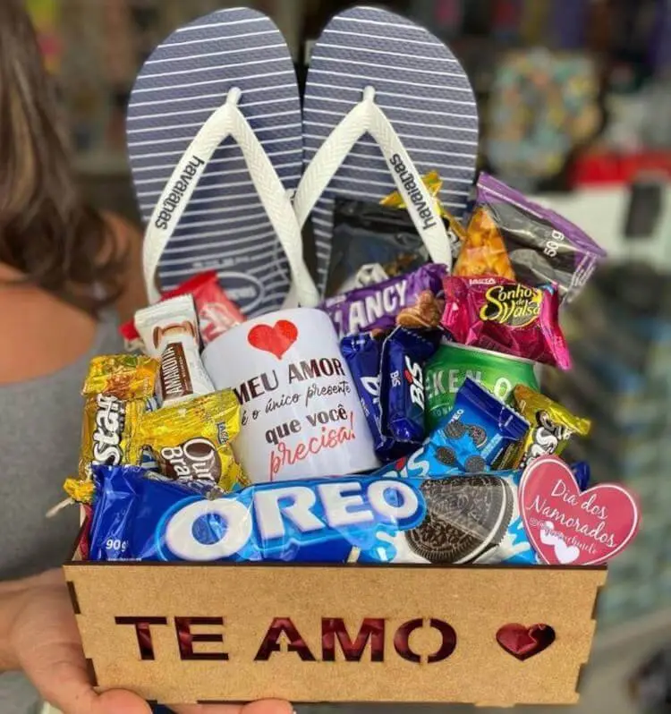 Cesta de madeira com chinelo azul e branco, doces e caneca com declaração