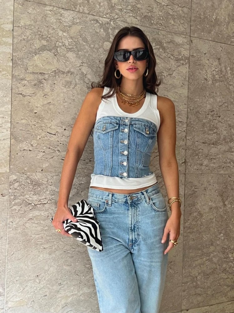 mulher usando regata branca com sobreposição com um corset jeans, usando calça jeans, clutch de zebra e óculos de sol preto