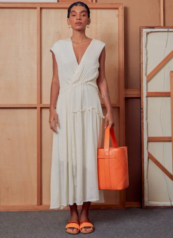 Modelo usa vestido branco e segura bolsa laranja