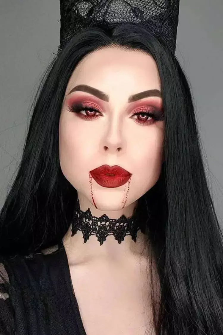 Mulher de pele clara com sombra vermelha, lente vermelha, batom vermelho e sangue falso escorrendo da boca