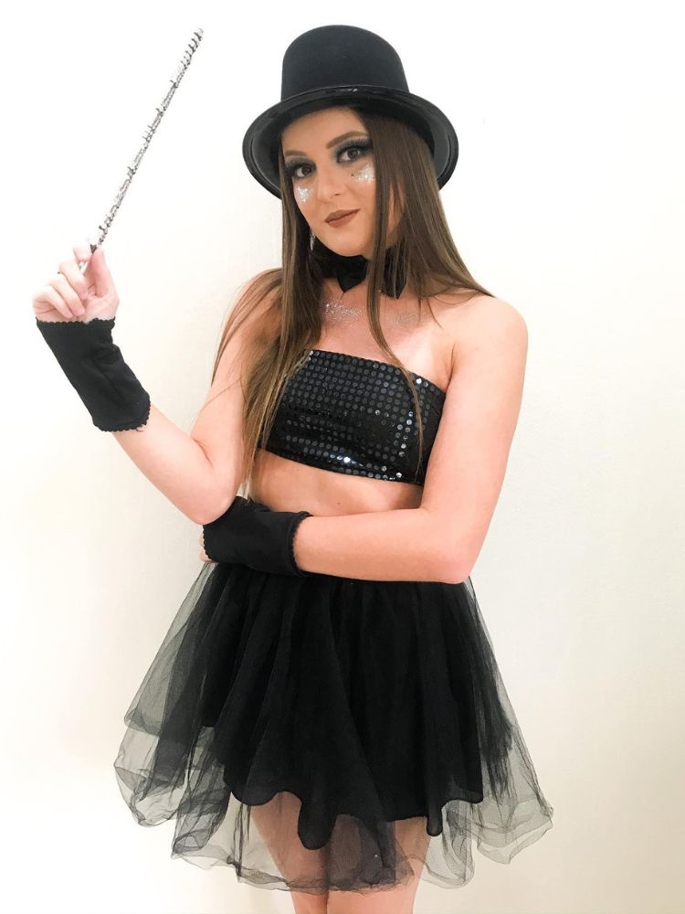 Mulher de pele clara de cartola, varinha, top preto e saia de tule preta
