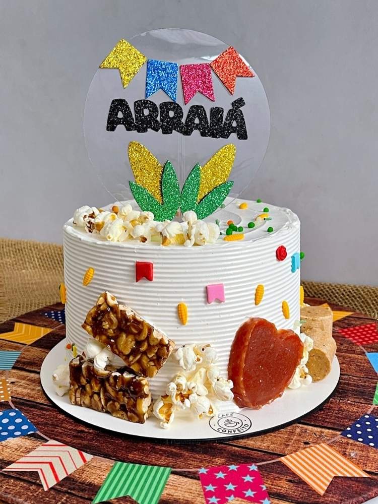 Bolo branco com enfeite de pipoca, pé de moleque, doce de abóbora e placa escrito "arraiá"