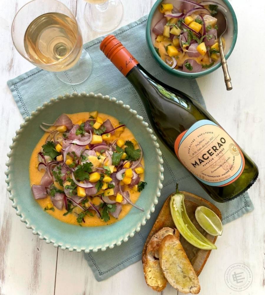 garrafa de vinho laranja Macerao sobre mesa ao lado de tigelas de ceviche, taça, torrada, pimenta e fatia de limão