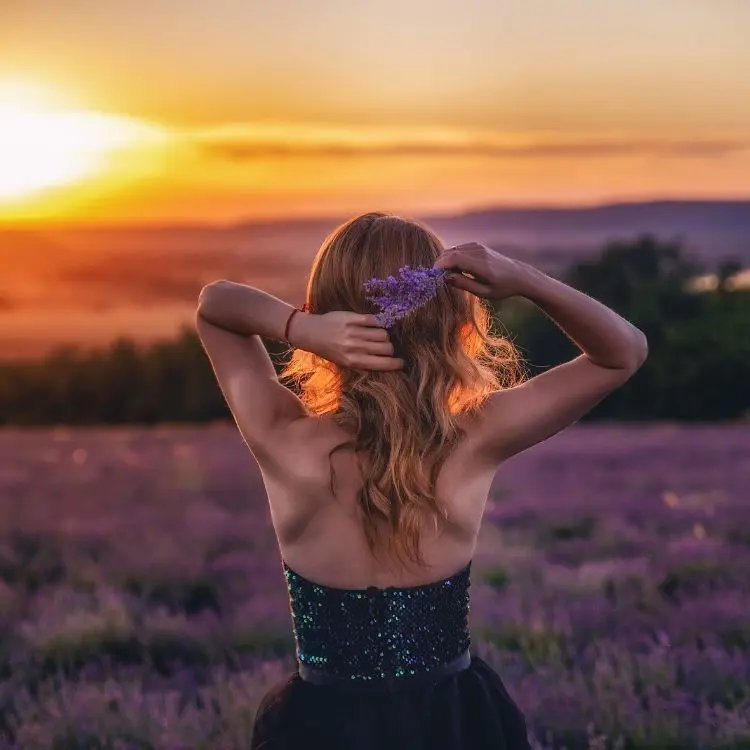 Mulher loira de costas ao por do sol em campo de lavanda