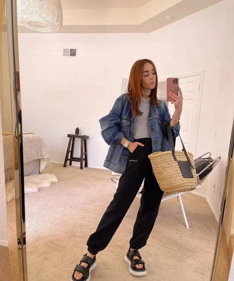 Uma mulher posa em um espelho ela usa uma calça de moletom, uma camiseta branca e uma jaqueta jeans