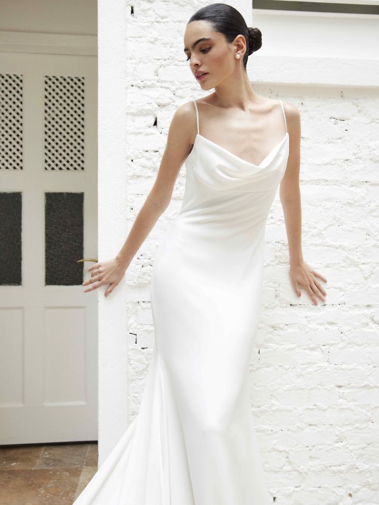Mulher de pele clara usando slip dress branco, com alcinhas e babado no colo, apoiada em parede branca. 