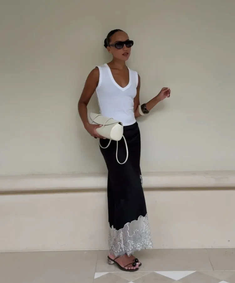 Foto de mulher morena usando regata  branca e saia de cetim preta, um dos looks para trabalhar no calor