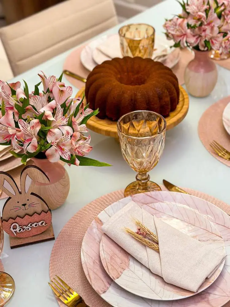 Mesa posta em tons de rosa com bolo ao fundo e enfeite de coelho