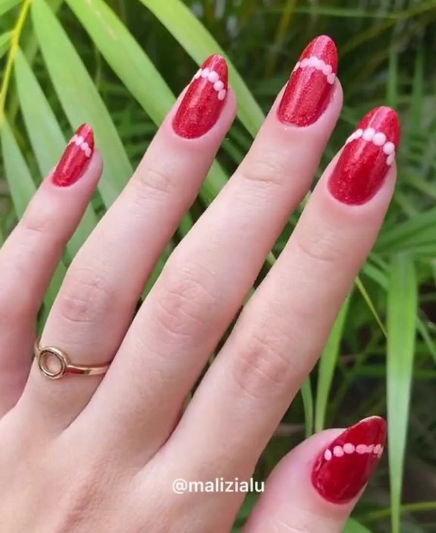 Mão de pele clara com unha almond em vermelho com glitter e bolinahs brancas 