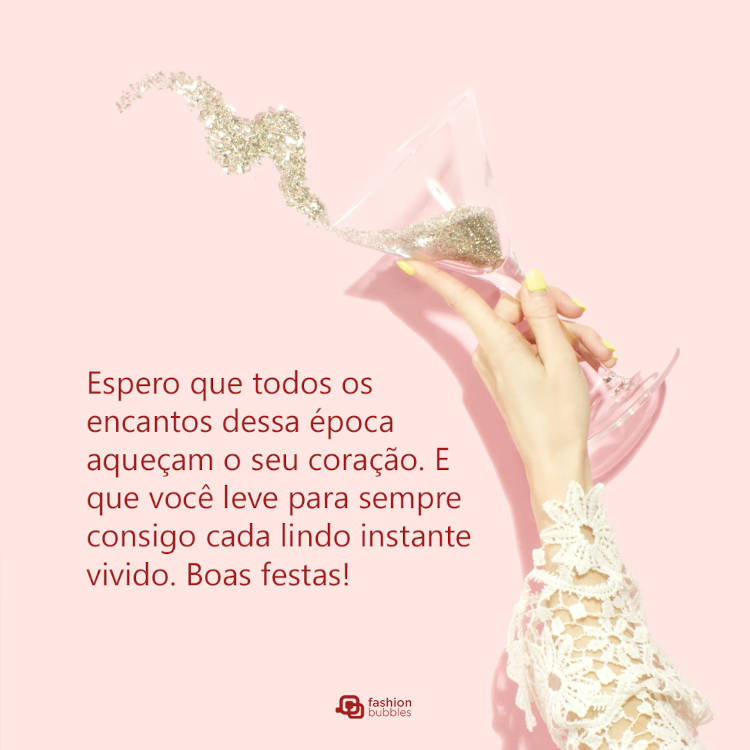 Foto de fundo pêssego com mulher de pele clara segurando taça com glitter e frase: Espero que todos os encantos dessa época aqueçam o seu coração. E que você leve para sempre consigo cada lindo instante vivido. Boas festas!