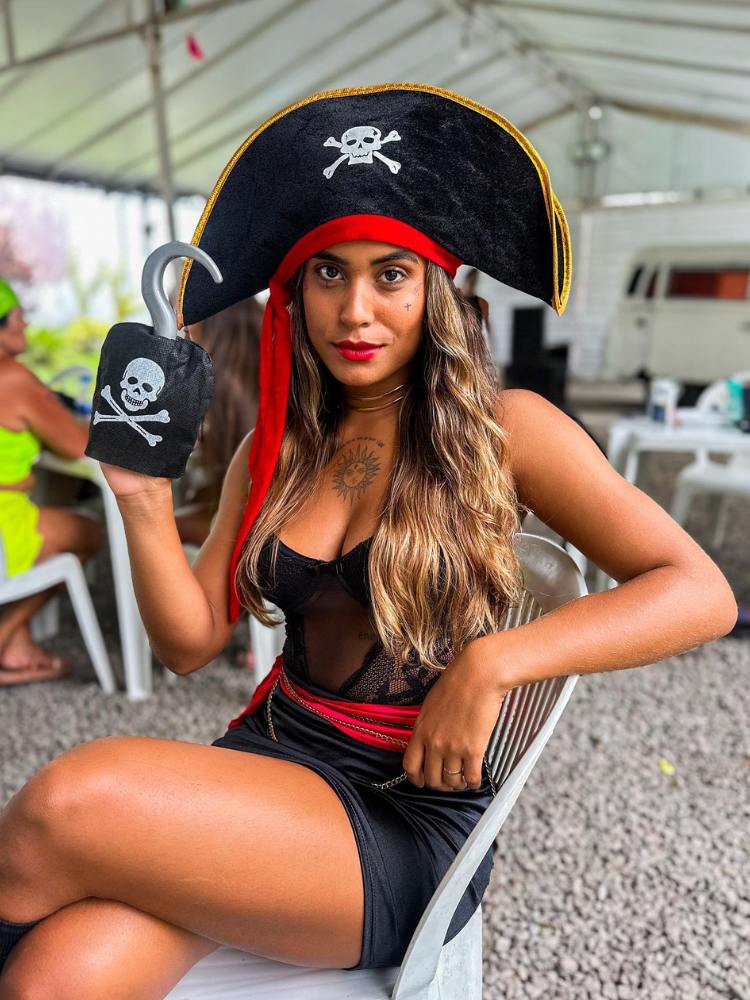 Mulher de pele morena com vestido preto, lenço vermelho, chapéu de pirata e mão de gancho