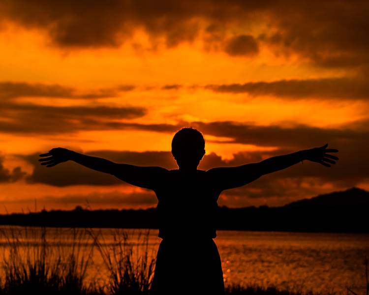 Mulher com os braços abertos no alvorecer do amanhecer. Foto de mulher - Reflexão de fim de ano.