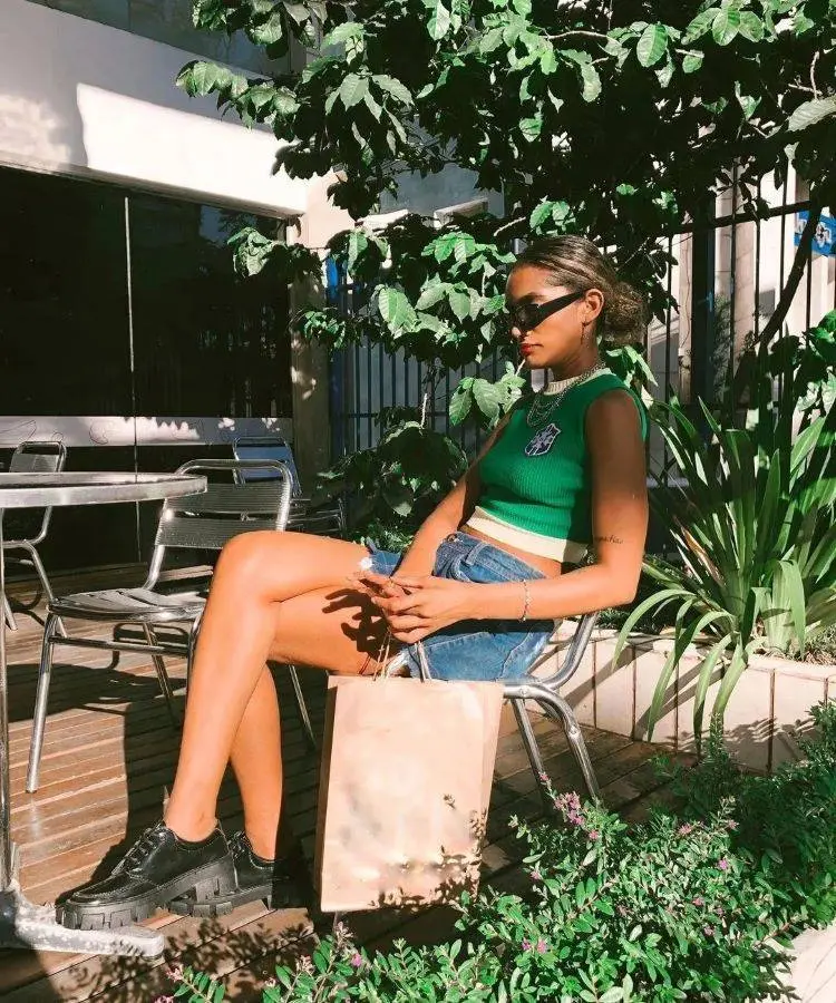 Colete de lã do Brasil com shorts jeans, tênis preto, mulher sentada em cadeira