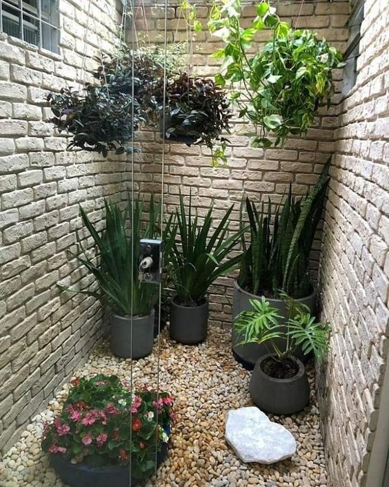 Jardim de inverno com paredes de tijolos à vista e vasos de diferentes tamanhos nas pedras e suspensos 
