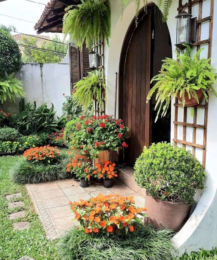 A imagem retrata um exuberante jardim florido, com uma variedade de plantas em tons vibrantes de roxo, lilás e verde. Um caminho sinuoso atravessa o cenário, rodeado por árvores altas, arbustos densos e flores coloridas, criando harmonia natural.