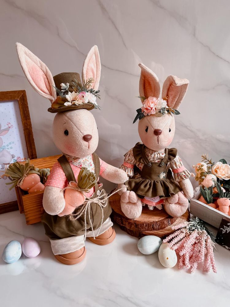 Dois coelhos feitos de tecido com roupas em marrom