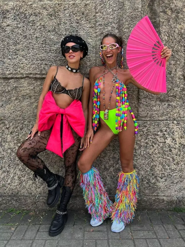 foto de duas amigas usando fantasia de Carnaval, uma usando top preto de renda e laço grande rosa na hot pant e outra usando top maximalista de miçangas e hot pant verde neon