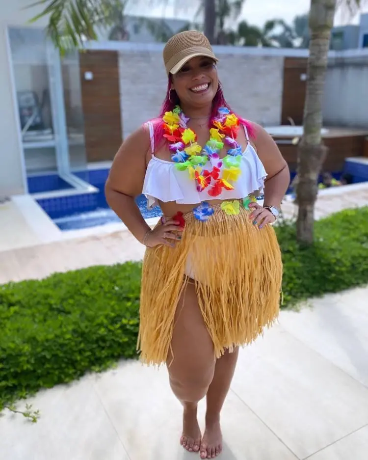 Mulher de pele morena com top branco, hot pant branca, saia de havaiana e colares de flor