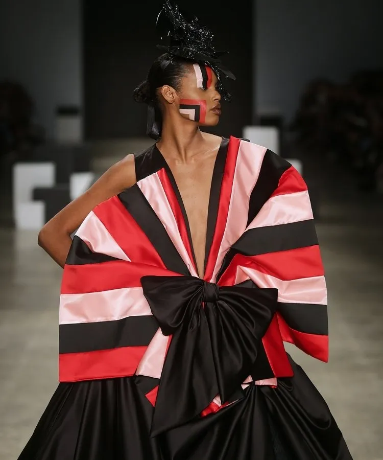 Foto de modelo na passarela usando vestido preto com laço listrado em rosa e vermelho