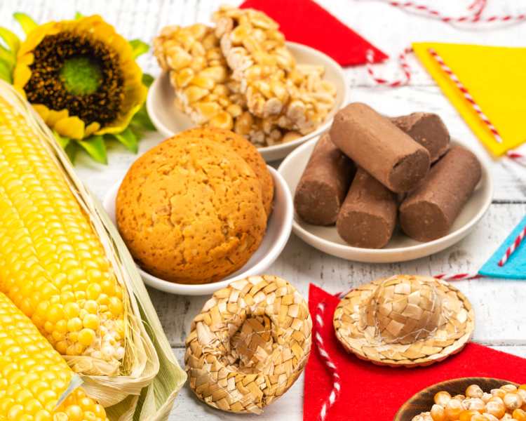Mesa com comidas tradicionais de festa junina, como broa de milho, pé de moleque, milho, paçoca, etc