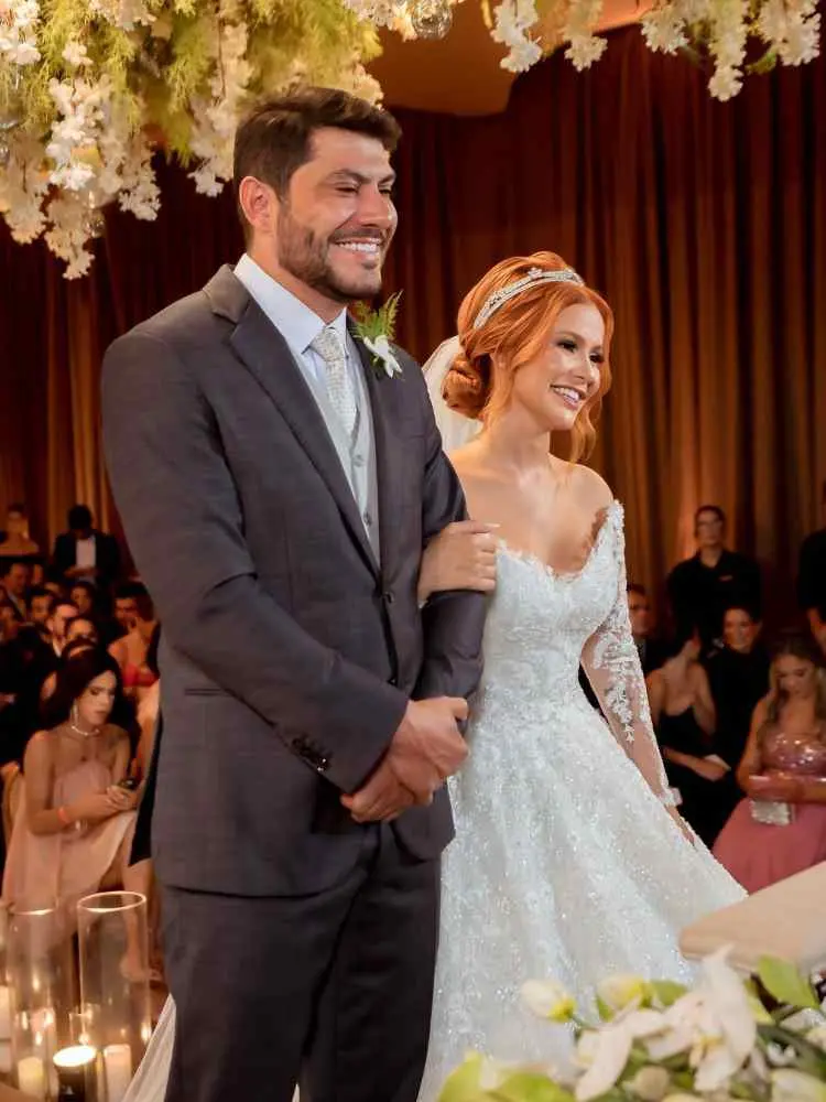 Noivo de Mirela sorrindo em seu Casório. Ele usa terno cinza-escuro.