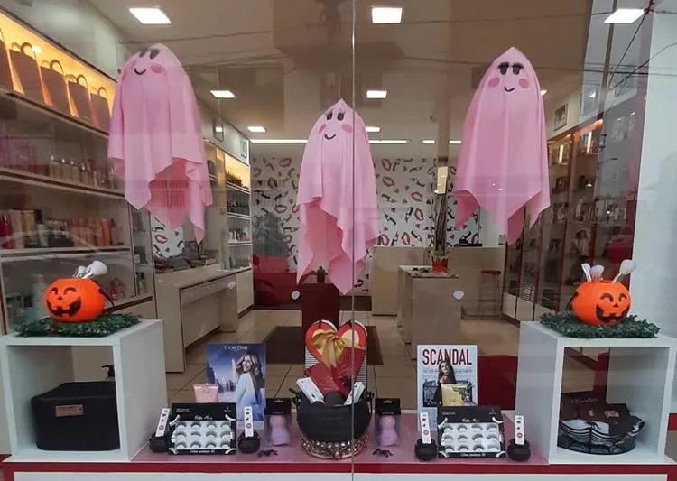 Vitrine de loja de maquiagem com produtos, pote de abóbora com pincéis e fantasmas de tecido rosa pendurados 