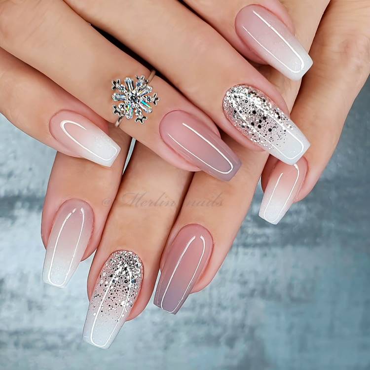 Unhas longas em formato quadrado decoradas com design elegante, incluindo degradê branco, glitter prateado e toques perolados. Um anel delicado em forma de floco de neve complementa o visual sofisticado. Fundo azul claro transmite suavidade e beleza.





