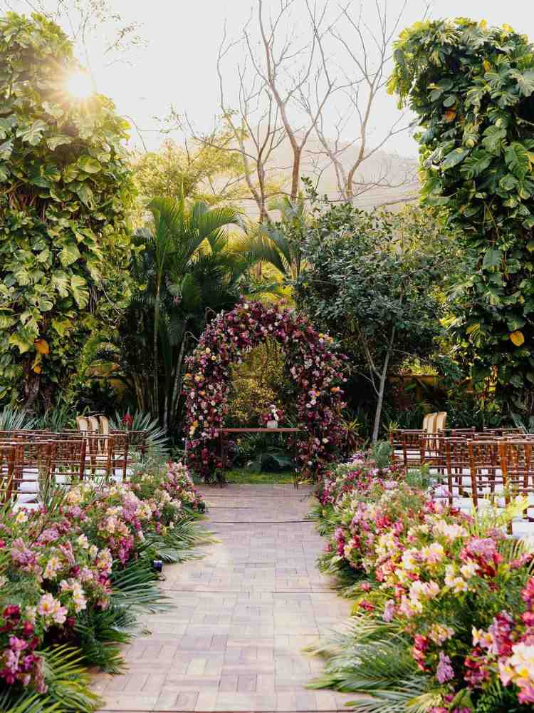 Decoração de casamento ao ar livre com muitas flores na entrada e no altar.