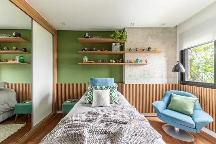 Quarto do filho mais novo, cores verde e tons neutros, cama com enxoval verde, azul e cinza. Poltrona azul com almofada verde. Acima da cabeceira da cama, prateleiras com plantas e bichinhos decorando