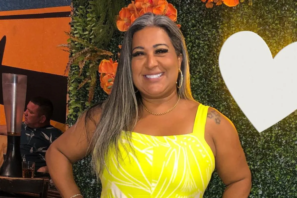 Mulher sorridente usando vestido amarelo em evento com painel decorativo de flores