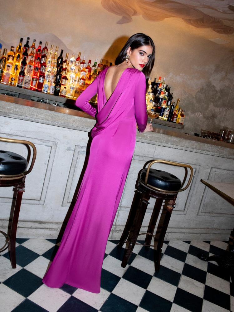 Mulher de pele clara  e de costas usando vestido violeta de manga longa e costas nuas 