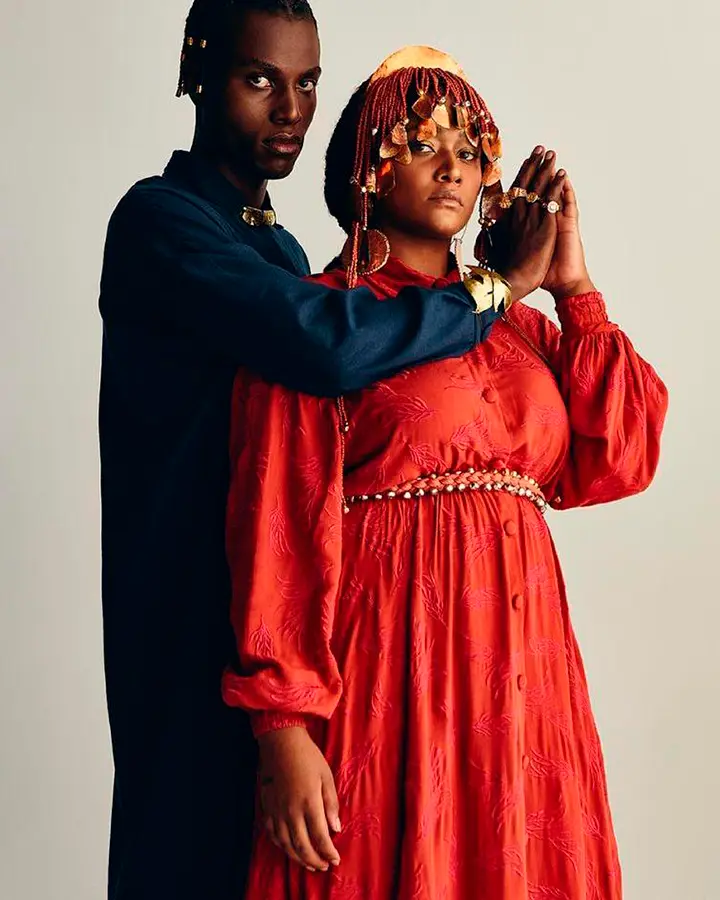 Casal de modelos, ele usa uma blus aazul, ela usa um vestido vermelho.