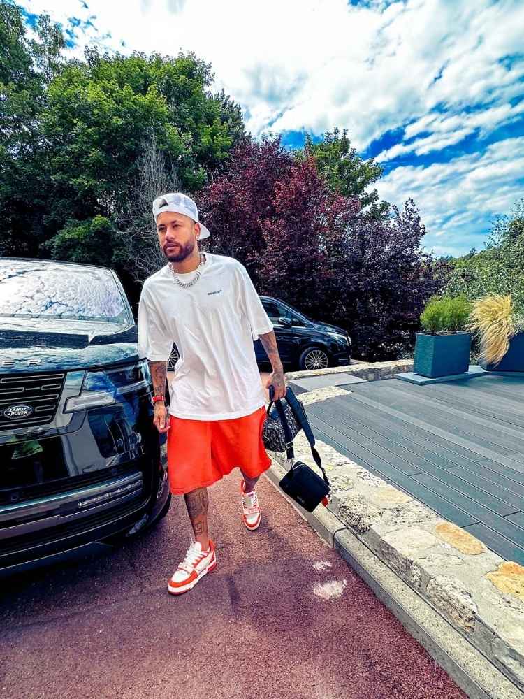 Neymar Jr usando blusa branca e bermuda laranja ao lado de Range Rover First Edition preta