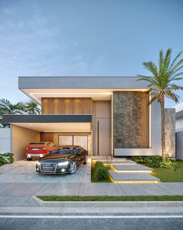 A imagem mostra uma casa moderna, com linhas retas, uma garagem aberta e um design exterior elegante. A casa tem iluminação interna que a destaca contra o céu escuro. Há um carro vermelho na garagem e outro preto na entrada. Há uma palmeira alta e um gramado bem cuidado na frente da casa.