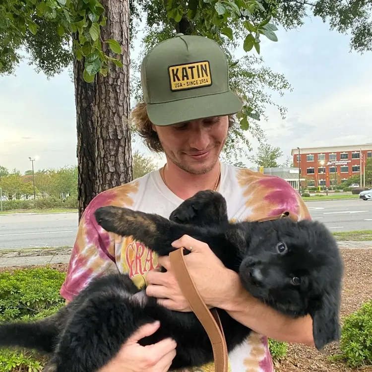 John B, personagem de "Outer Banks", com cachorro. Foto de John B usando boné.