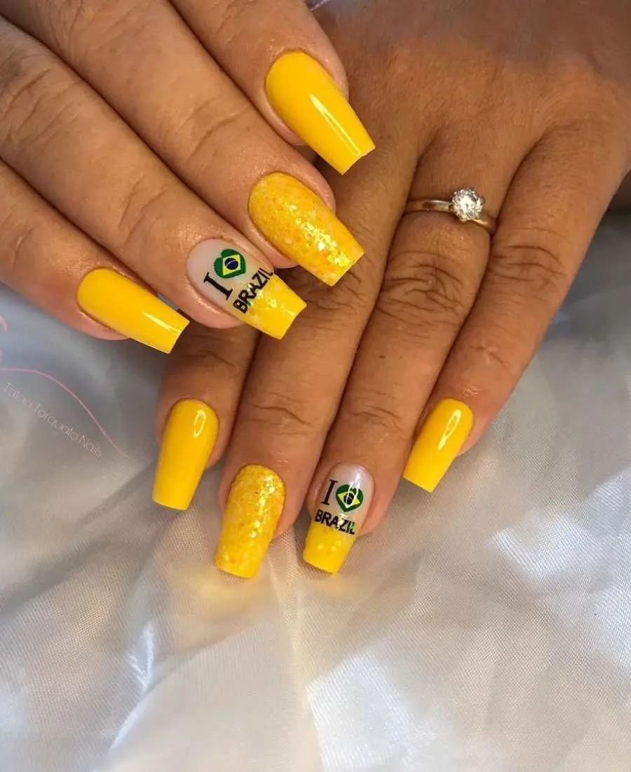 Imagem de mão decoradas com esmalte. Cores usadas, amarelo e glitter amarelo. Polegar, indicador e mínimo, amarelo. Médio, amarelo com glitter. Anelar, francesinha amarelo com glitter + adesivo "I Love Brazil". 