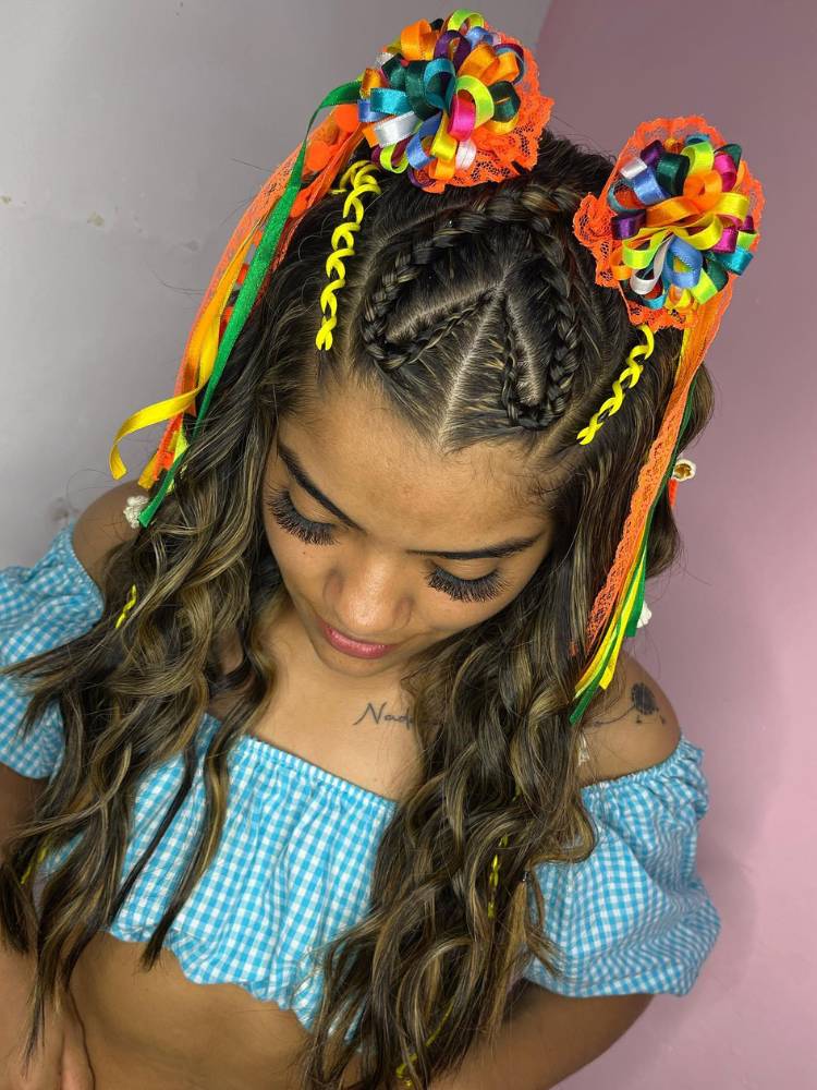 Mulher de pele negra usando blusa azul e penteado de festa junina, com tranças, cabelo solto e enfeites coloridos