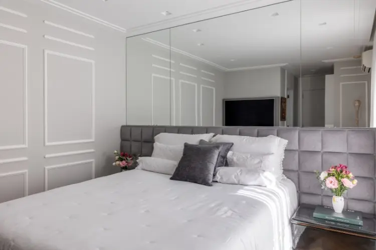 Quarto com cama de casal, espelho grande atrás da cama e boiserie nas paredes 