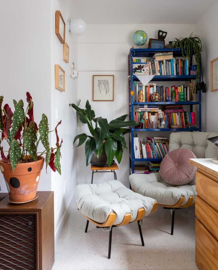 canto de sala com poltrona grande branca, dois vasos de planta perto e estante azul com livros