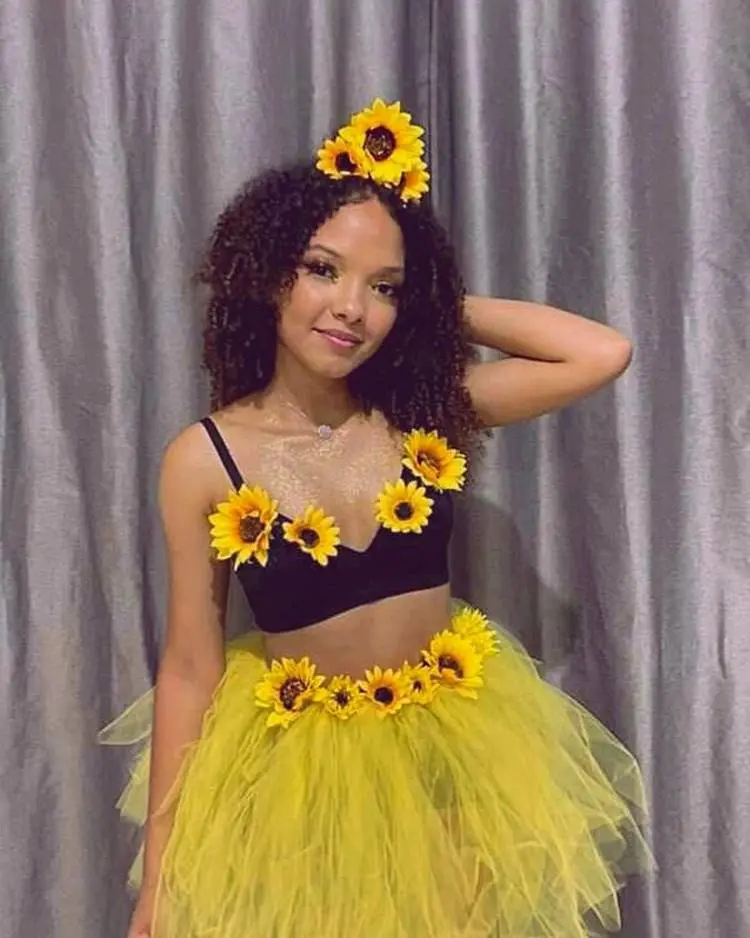 Mulher de pele morena com top preto, saia amarela enfeitados de girassol