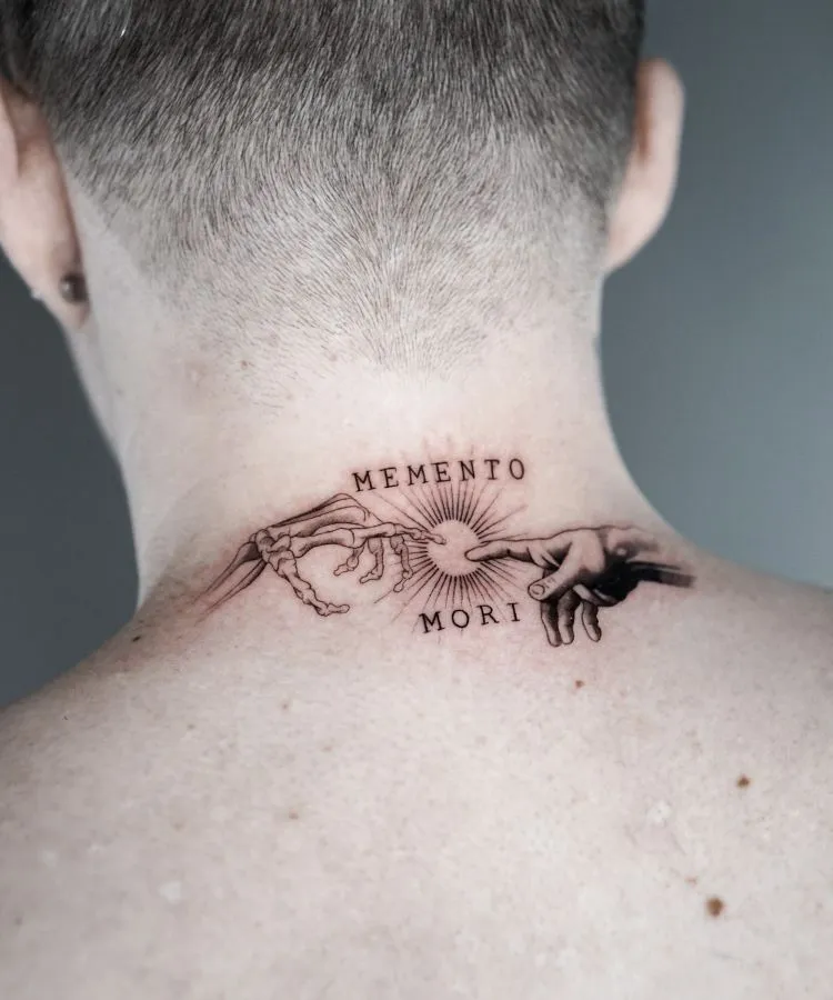 A imagem mostra uma pessoa de costas com cabelo curto. Ela tem uma tatuagem no pescoço que representa duas mãos se tocando, uma esqueleto e outra humana, com as palavras "Memento Mori" acima e abaixo. A tatuagem é detalhada em preto e ocupa a parte superior das costas.