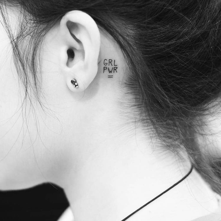 Foto em preto e branco de tatuagem pequena "GRL PWR" atrás da orelha, em fineline 