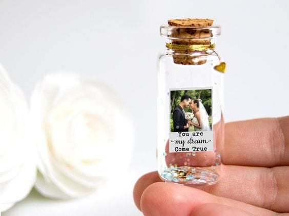 Mão segurando potinho de vidro com foto de casal