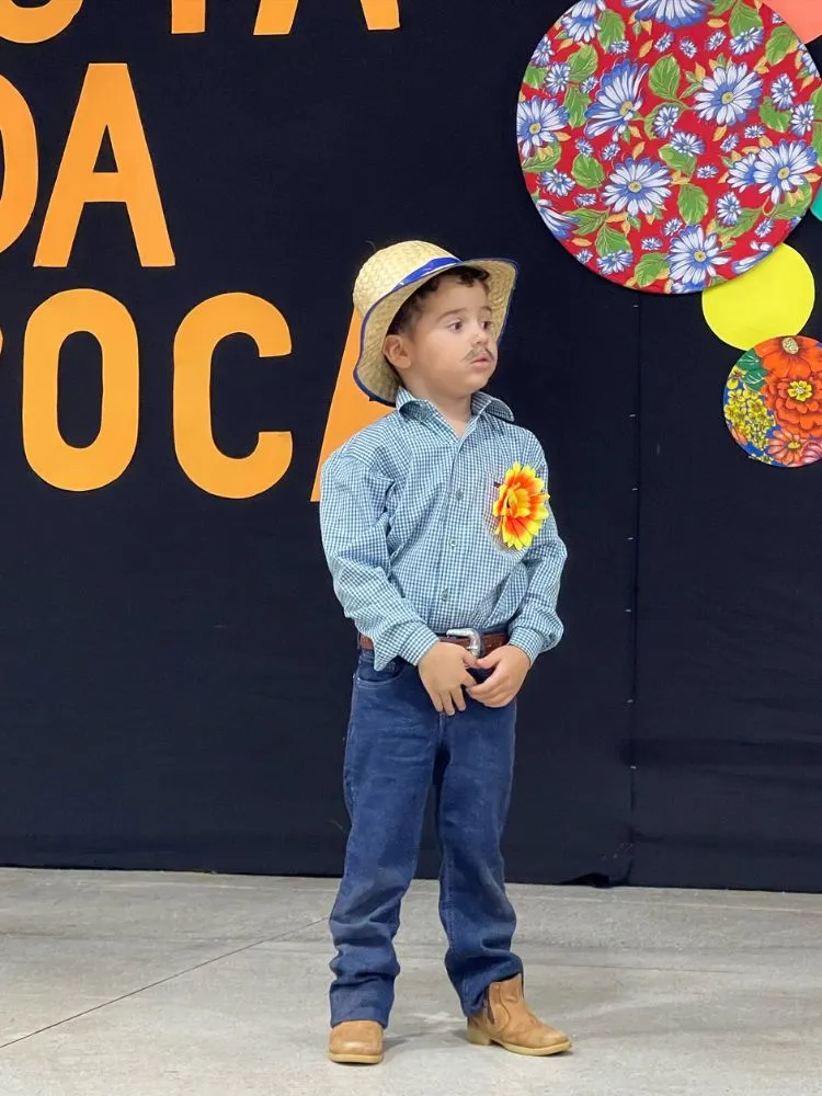 Menino de camisa xadrez, calça jeans, chapéu e broche de girassol 